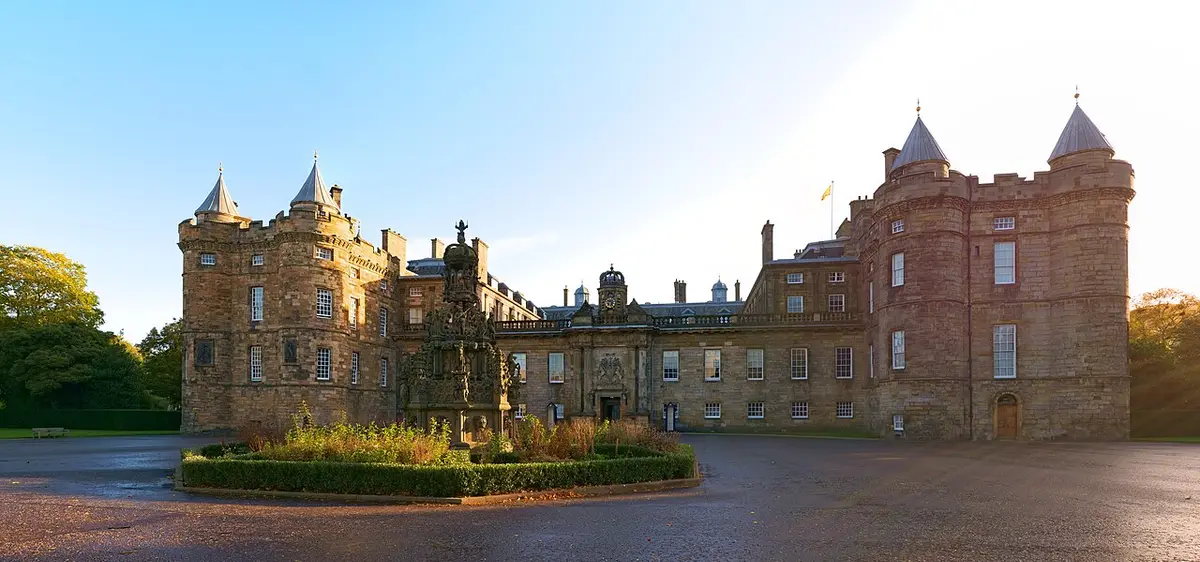 The front of the Palace of Holyroodhouse, with round corner towers and a stone fountain in the forecourt