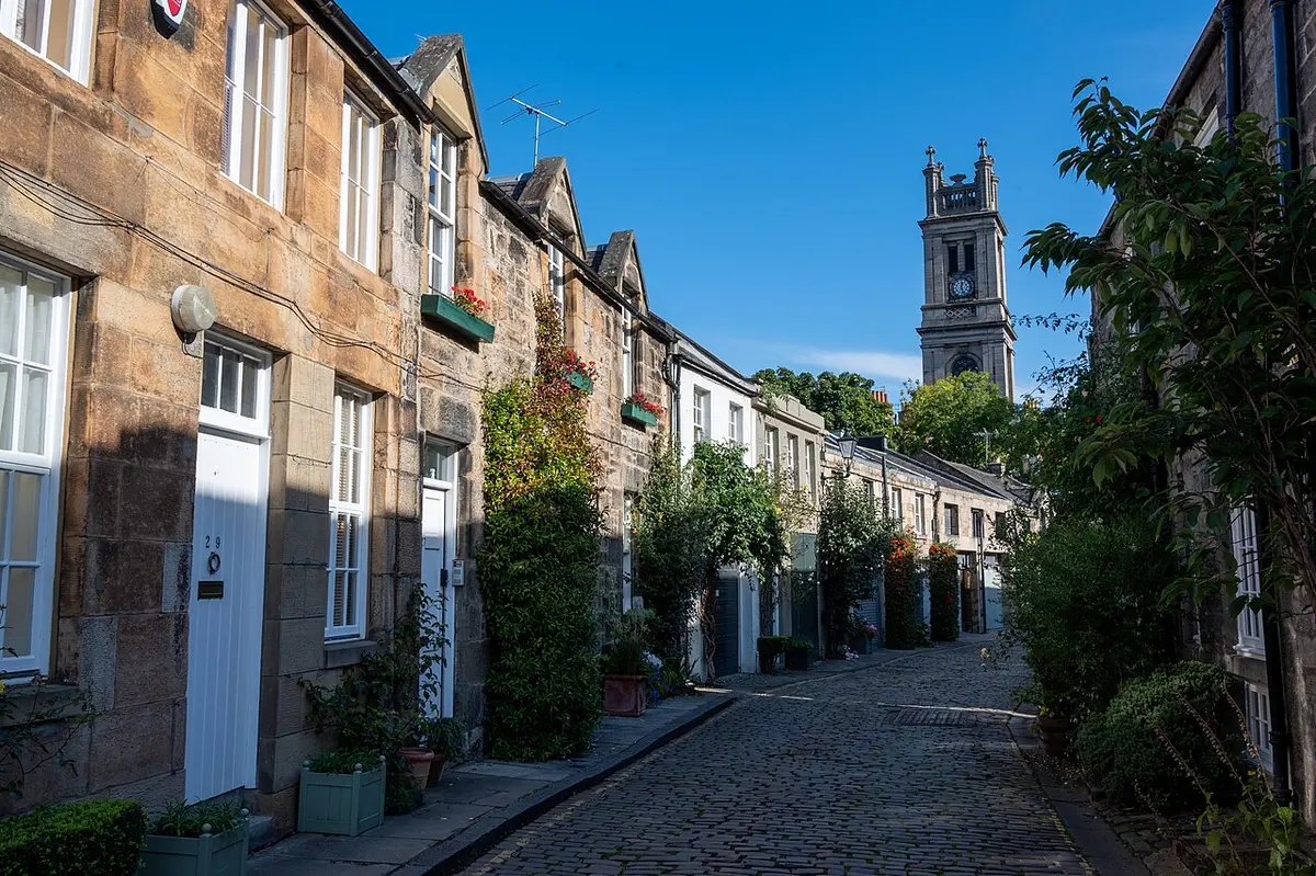 Circus Lane, a curving cobbled mews of stone houses with plants at the doors, a church clock tower at the end