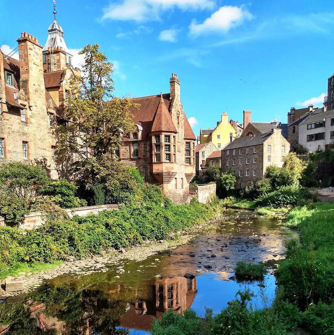 Old mill buildings and Well Court’s red roofs above the Water of Leith in Dean Village on a sunny day