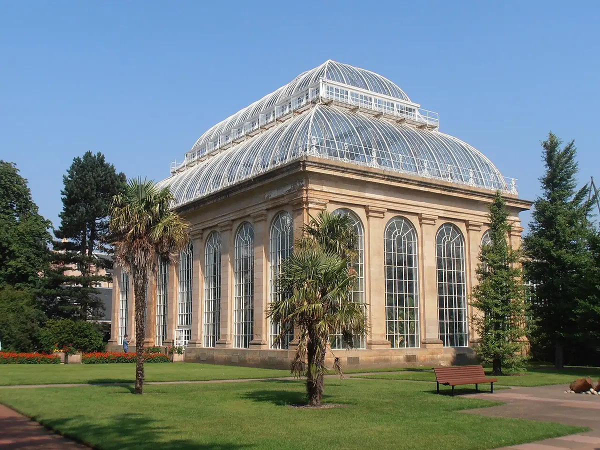 The stone and glass Victorian Palm House at the Royal Botanic Garden, with palms on the lawn in front