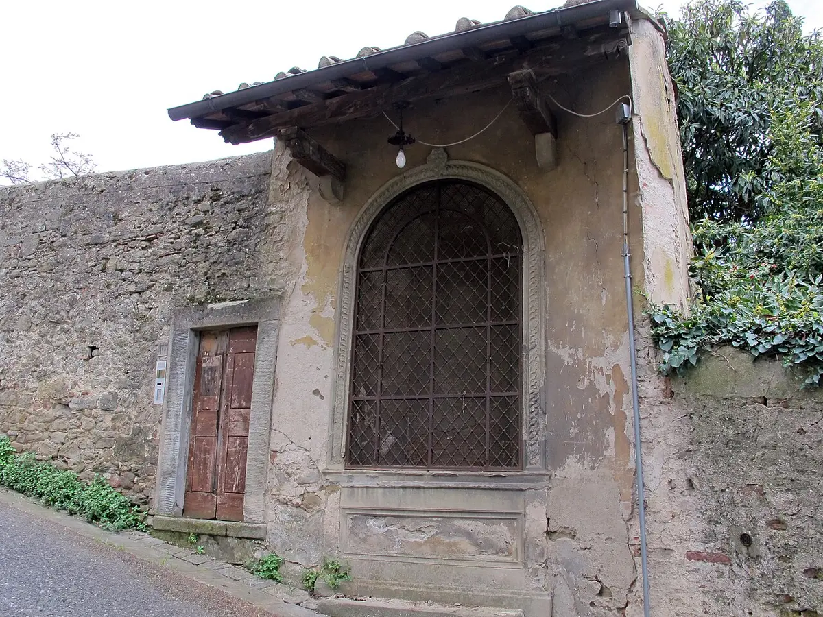A small roofed wayside shrine set into a stone wall beside the steep Via Vecchia Fiesolana