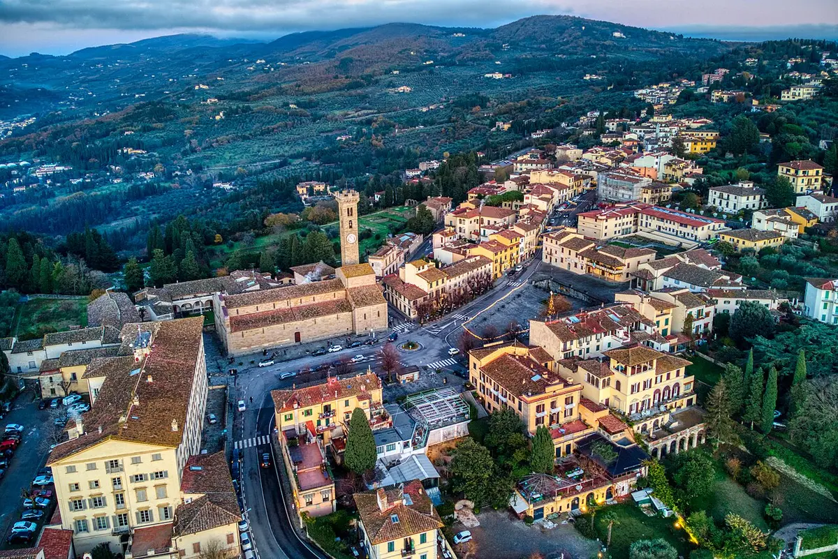 Aerial view of Fiesole’s main square and its cathedral with a tall bell tower, olive-covered hills beyond