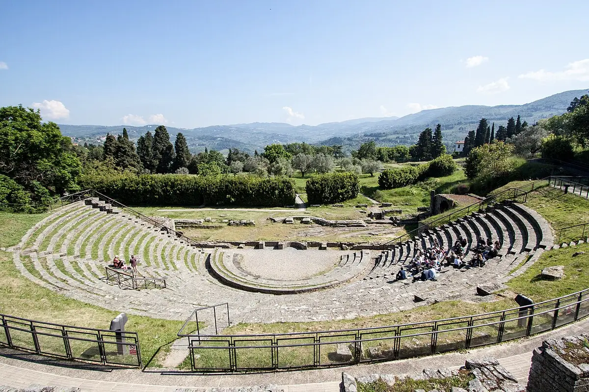 The stone seats of the Roman theater at Fiesole curving around its stage, wooded hills behind