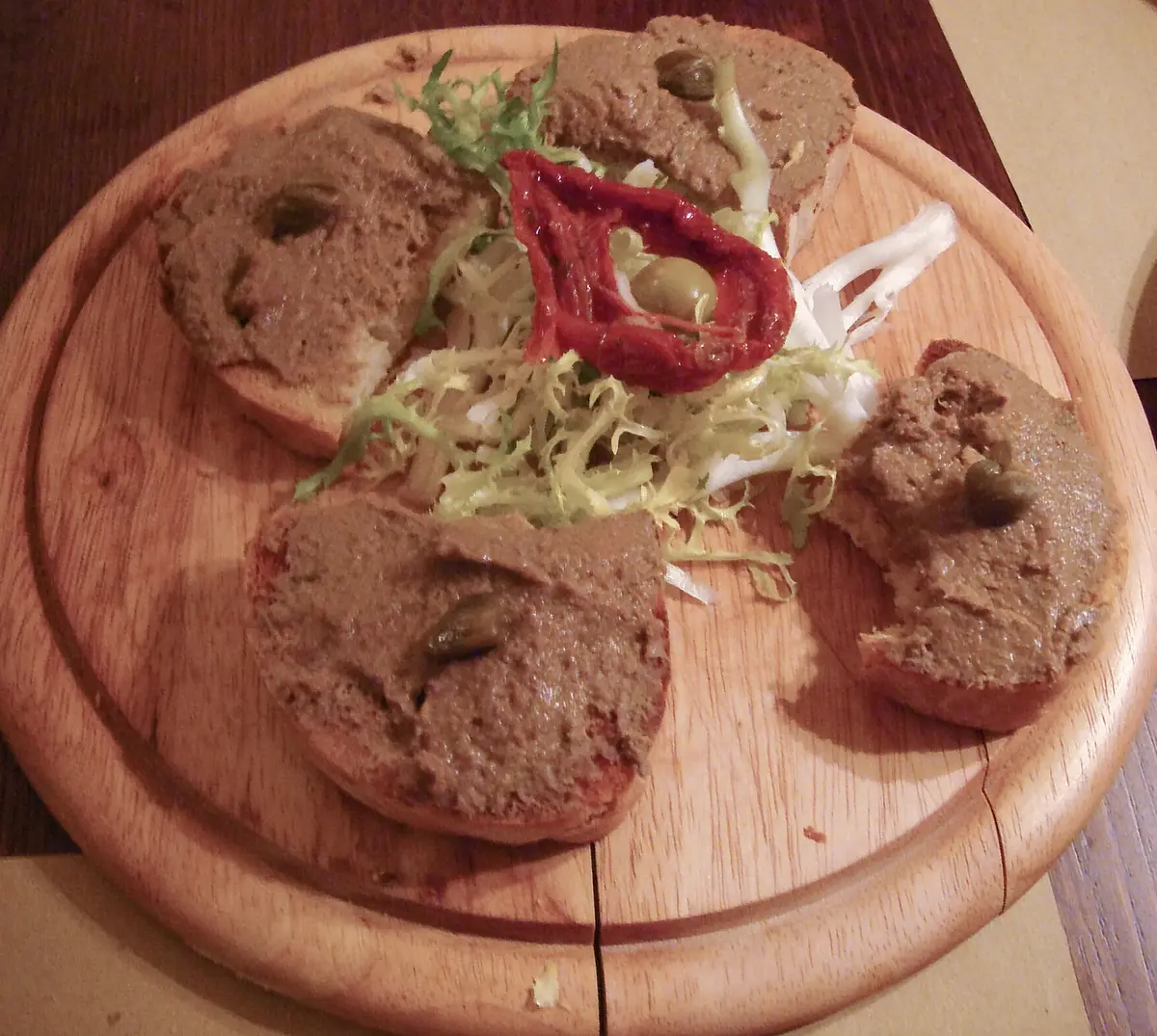 Slices of toasted bread spread with chicken liver pâté on a wooden board
