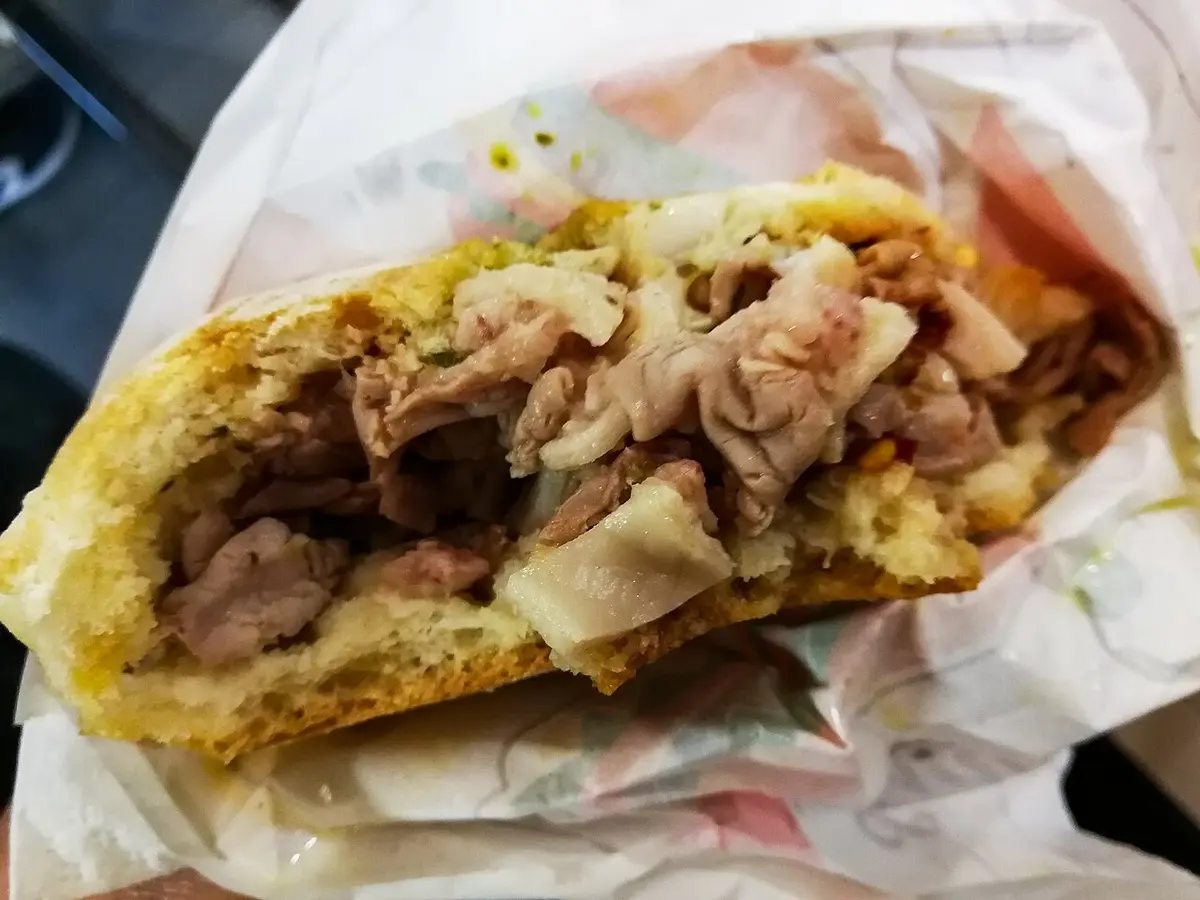 A lampredotto sandwich, sliced tripe and green sauce in a bread roll, wrapped in paper