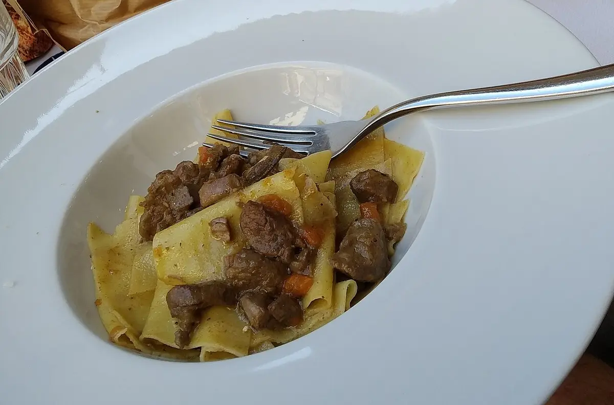 Wide pappardelle with pieces of wild boar ragù on a white plate