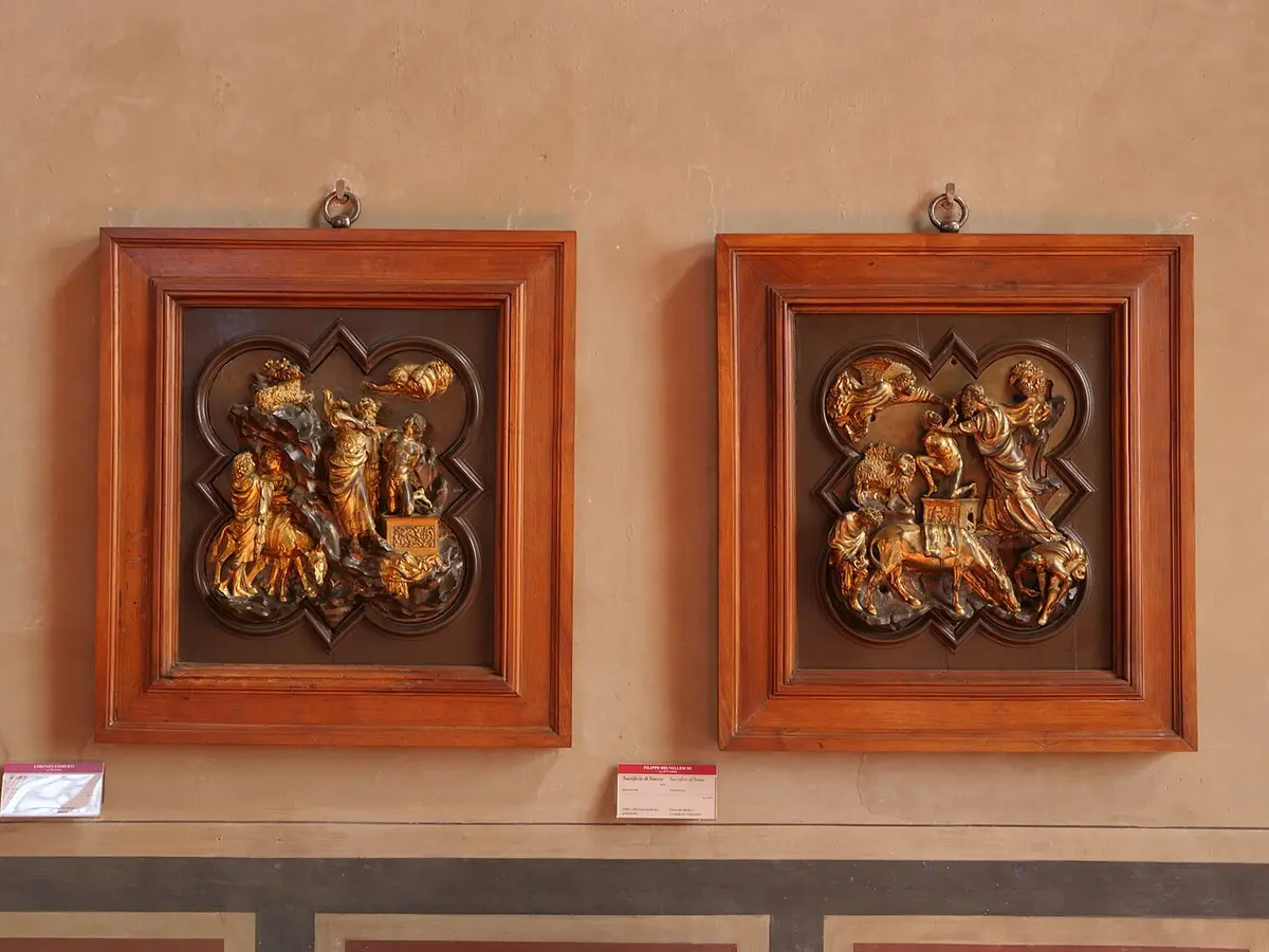 Two gilded bronze reliefs of the sacrifice of Isaac in quatrefoil frames, side by side on a museum wall