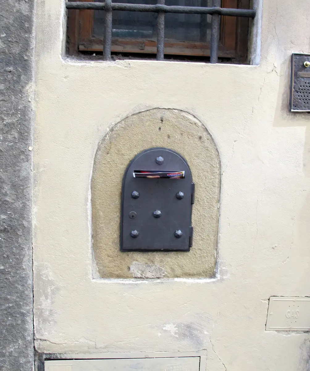 A small arched wine window with an iron door in a stone frame, set in a cream-colored wall