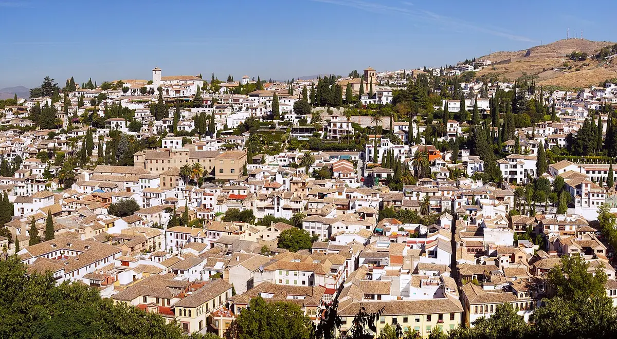 The white houses, cypresses and church towers of the Albaicín covering a hillside under a blue sky