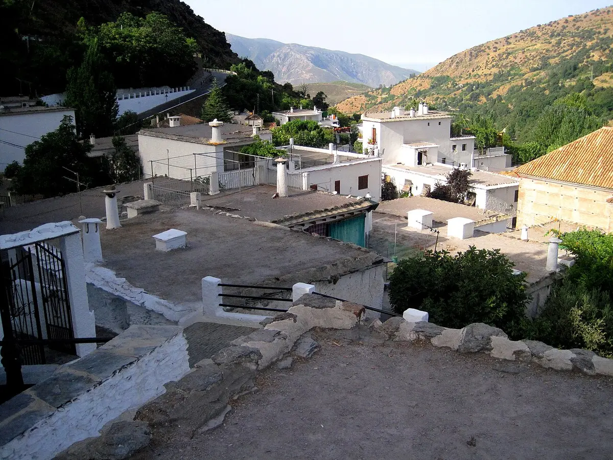 Flat grey clay roofs with round white chimneys in Pampaneira, mountains behind