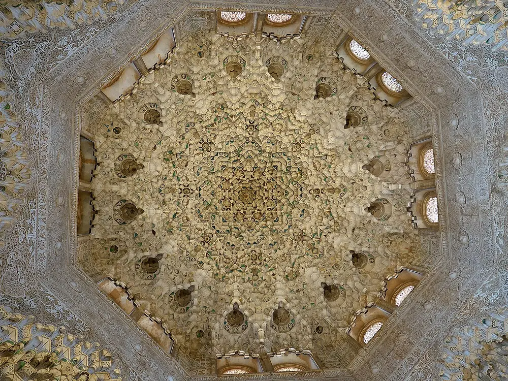 Looking up into an octagonal dome made of thousands of small carved plaster cells, with windows around its base