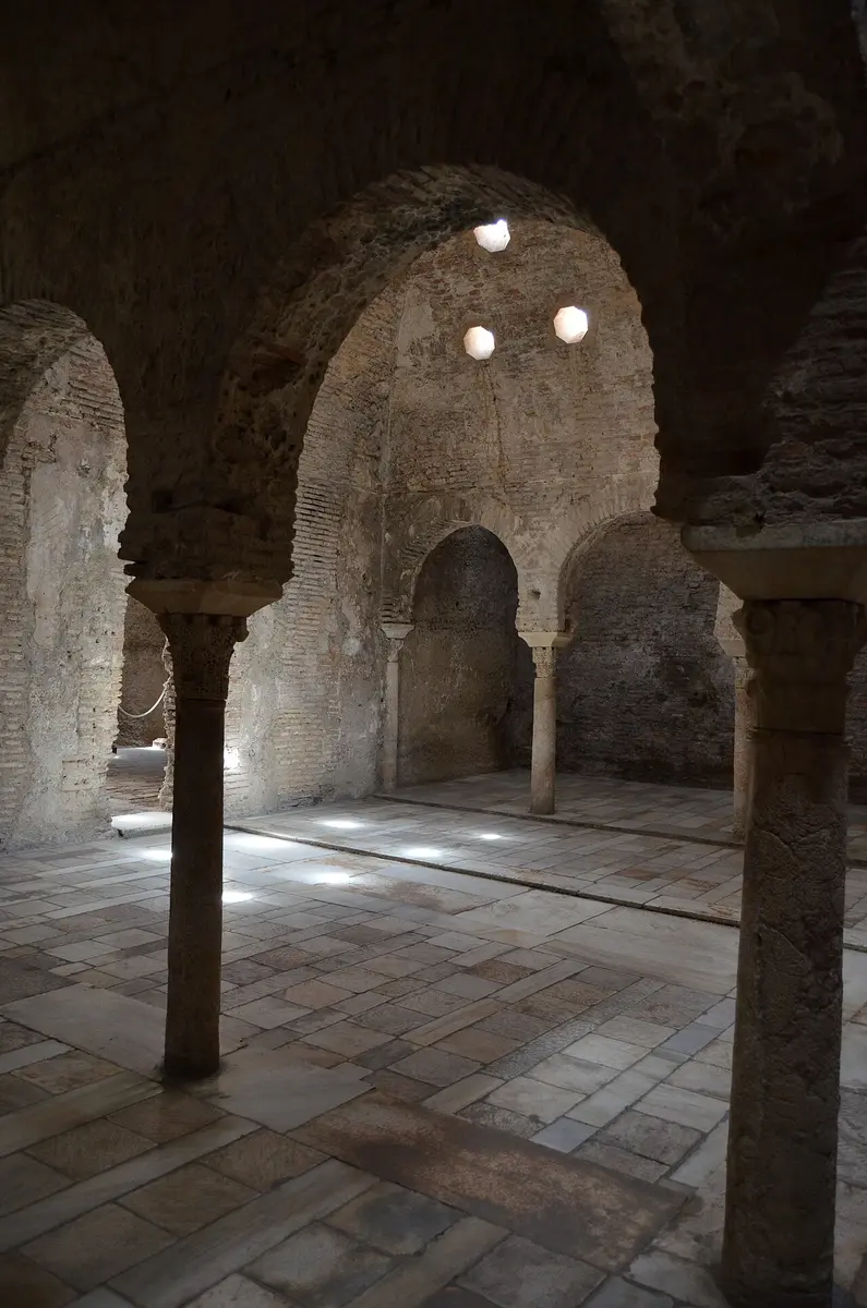 Brick horseshoe arches on stone columns inside the old Arab baths, lit through star-shaped openings in the vault