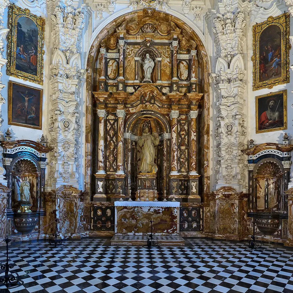 The baroque sacristy of the Cartuja, white stucco and colored marble around a gilded altar, over a checkered floor
