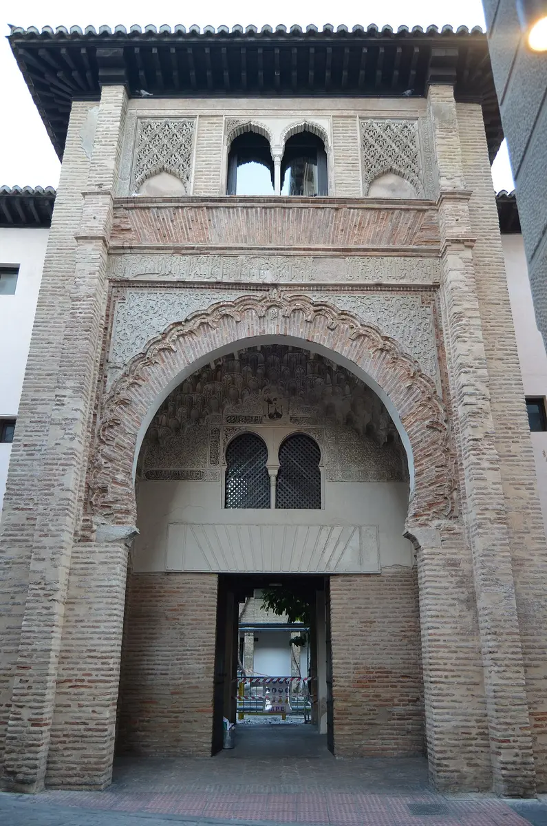 The tall horseshoe-arched brick gateway of the Corral del Carbón, carved plaster inside the arch