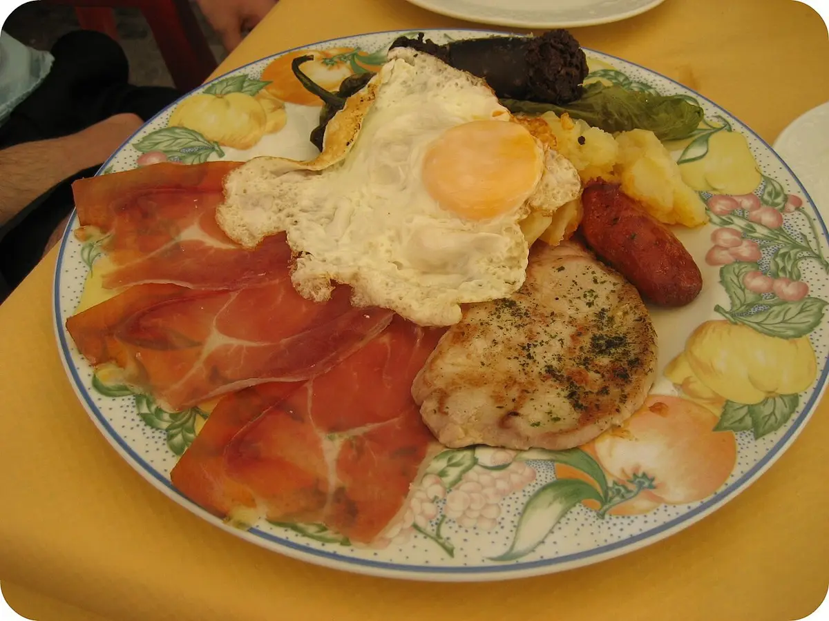 A plate of cured ham, a fried egg, sausages, a slice of pork and fried potatoes