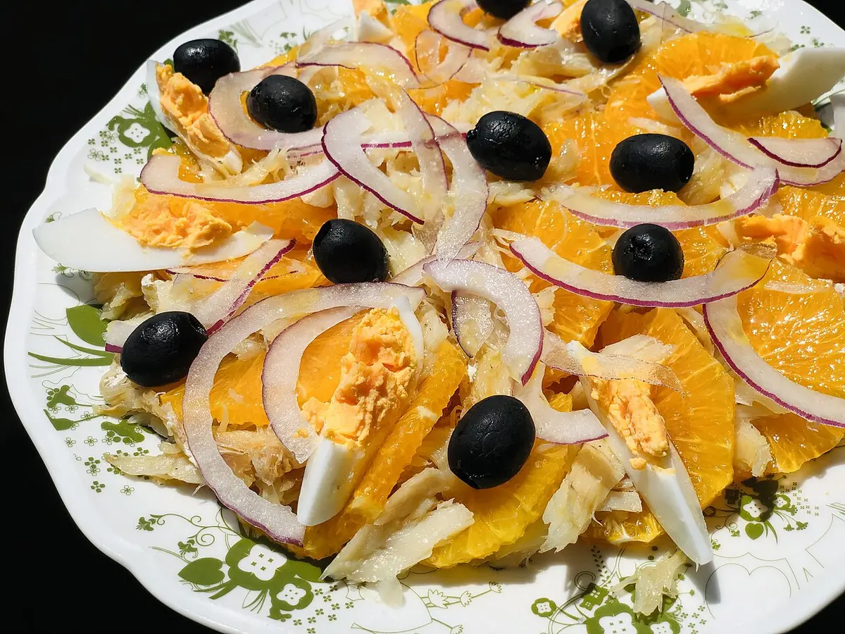 A salad of orange slices, salt cod, red onion and black olives on a patterned plate