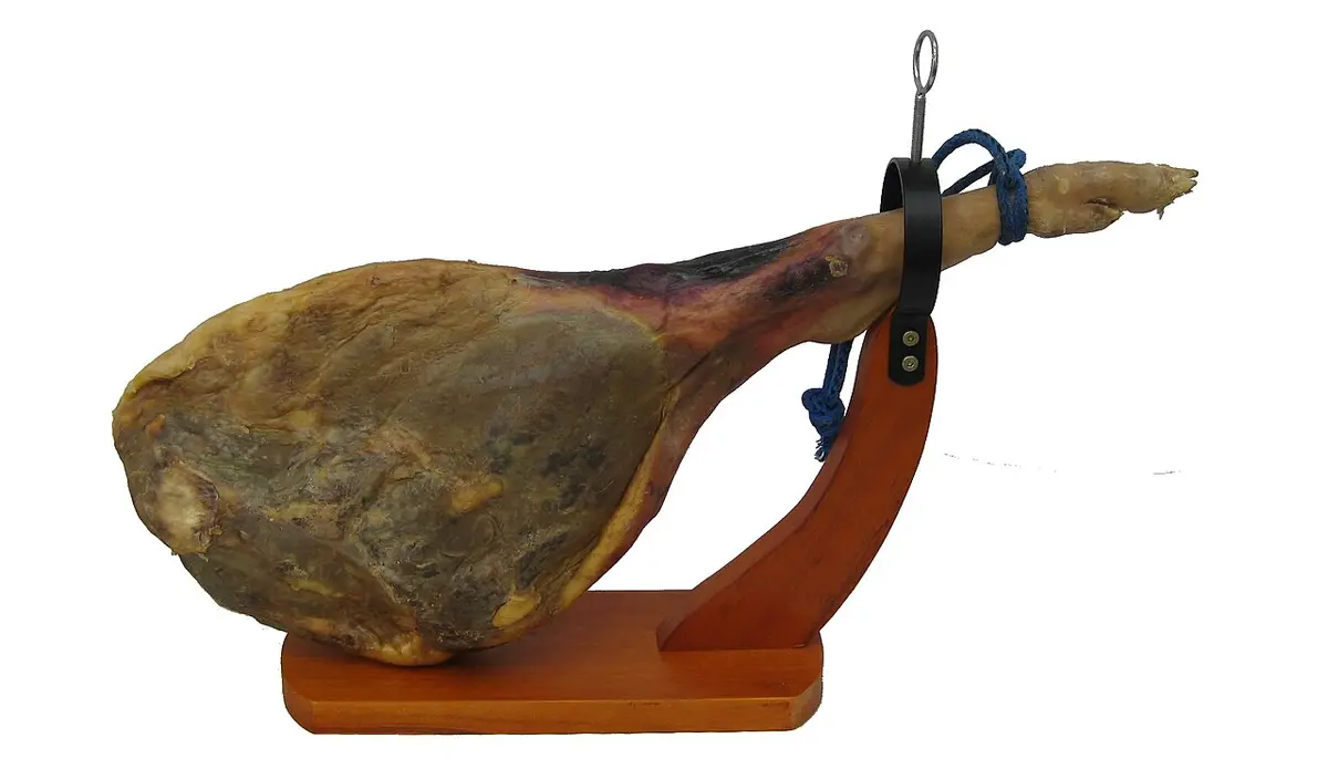 A whole cured ham held in a wooden ham stand