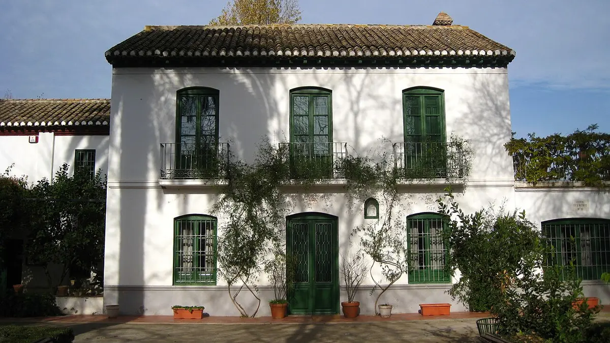 A white two-story farmhouse with green shutters and climbing plants