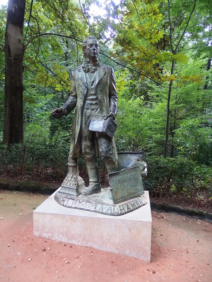 A bronze statue of Washington Irving holding a book, among trees in the Alhambra woods