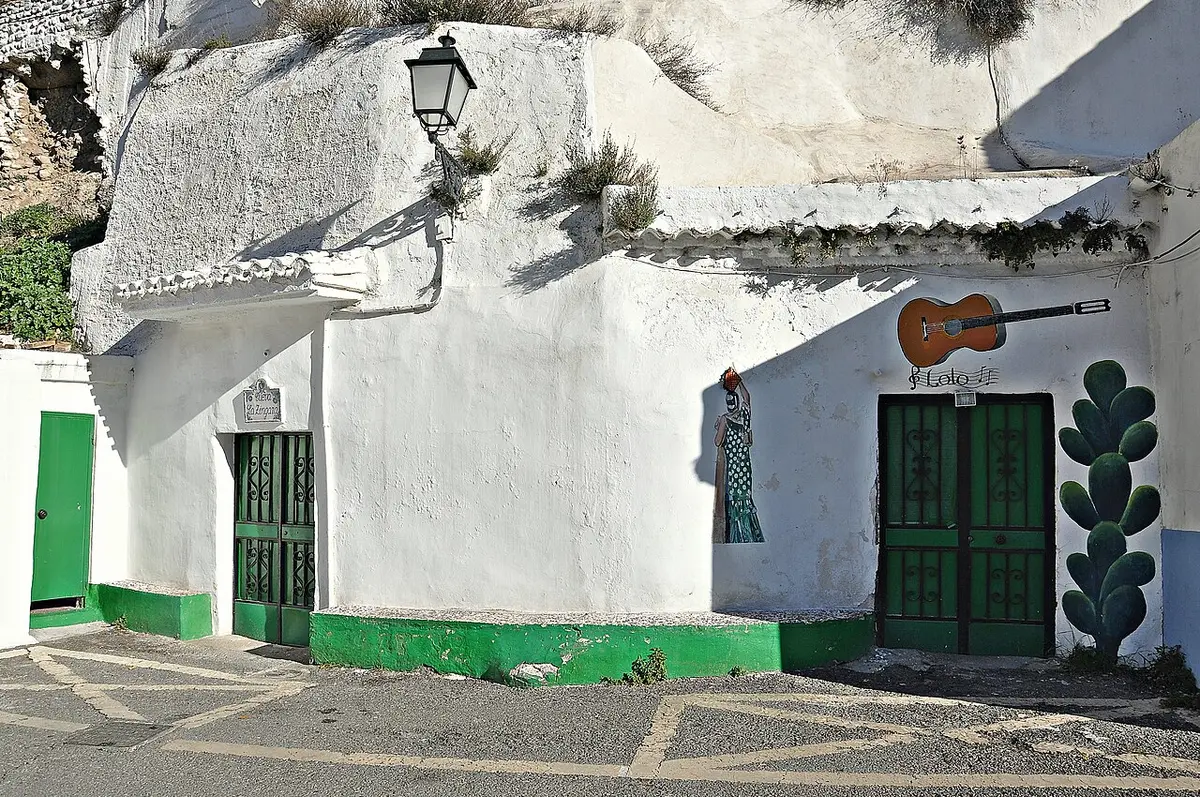 Whitewashed cave houses dug into a hillside, with green doors and a painted guitar on the wall