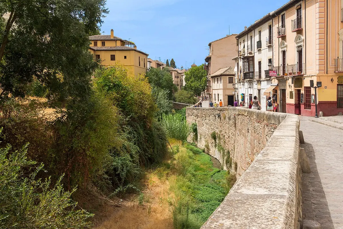 The narrow Darro river below a stone parapet and tall old houses on the Carrera del Darro