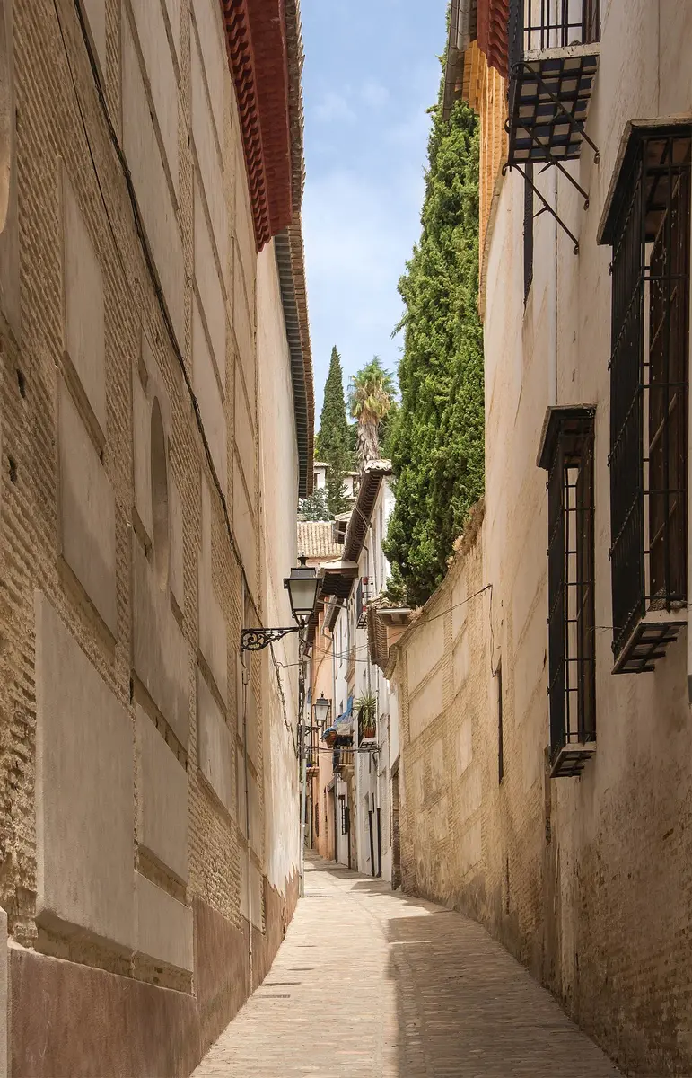 A narrow cobbled lane between high whitewashed and brick walls in the Albaicín, cypresses at the end