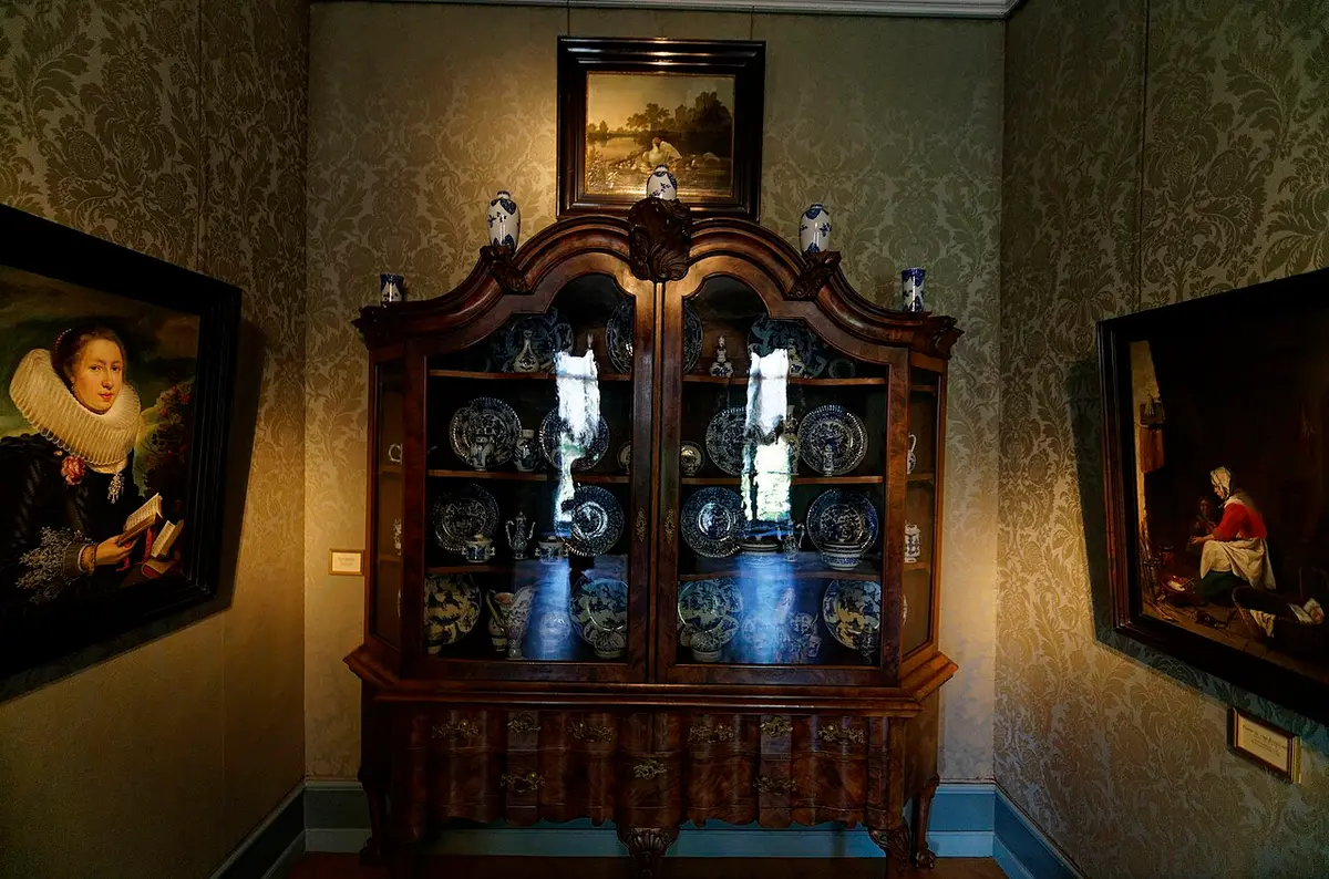 A room in Museum Bredius with a walnut cabinet of blue and white porcelain between 17th-century paintings on damask walls