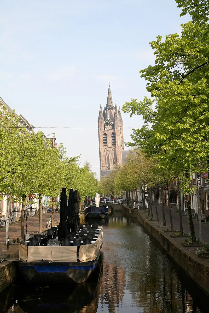 The leaning brick tower of the Oude Kerk at the end of the tree-lined Oude Delft canal