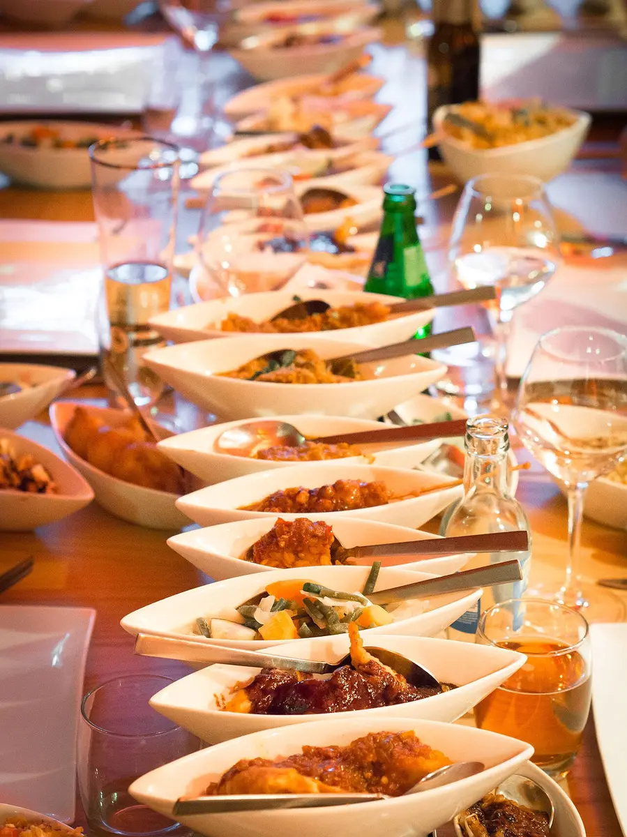 A long restaurant table covered with small bowls of Indonesian dishes around rice, lit by candles