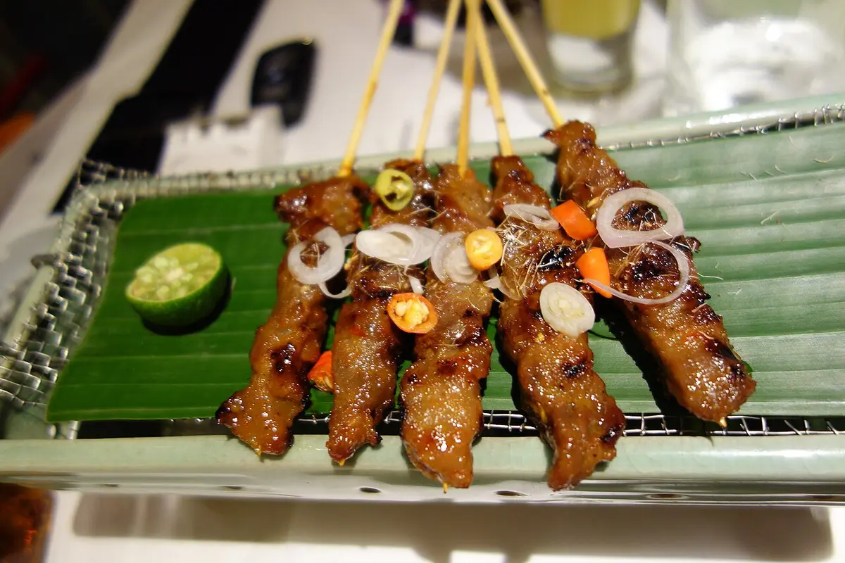 Skewers of grilled chicken satay on a banana leaf with lime and sliced shallots