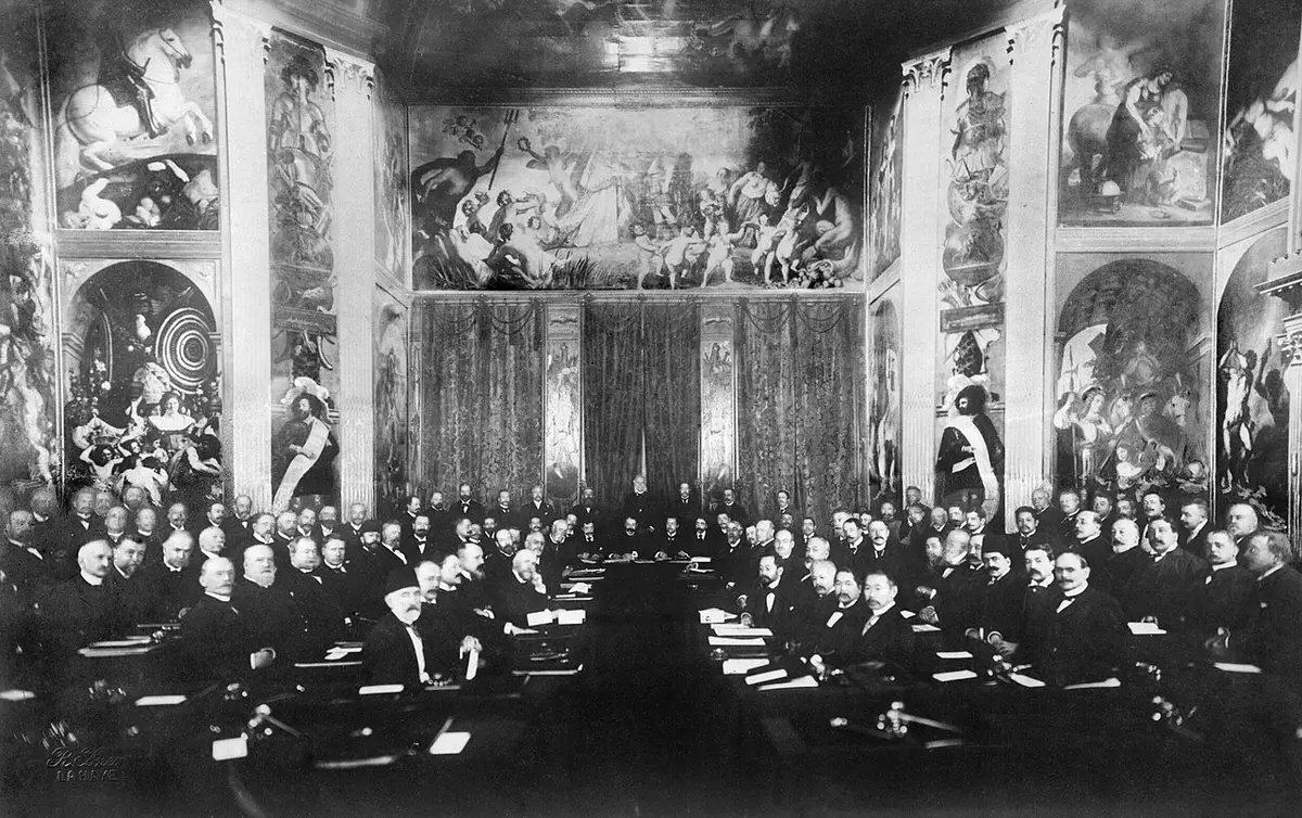 Black and white photograph of delegates seated at long tables in a hall with painted walls