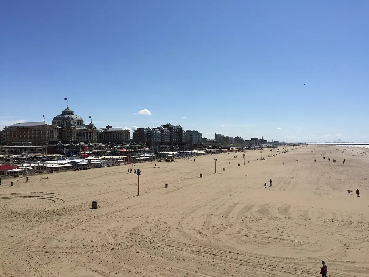 The wide sandy beach at Scheveningen under a blue sky, the domed Kurhaus in the distance