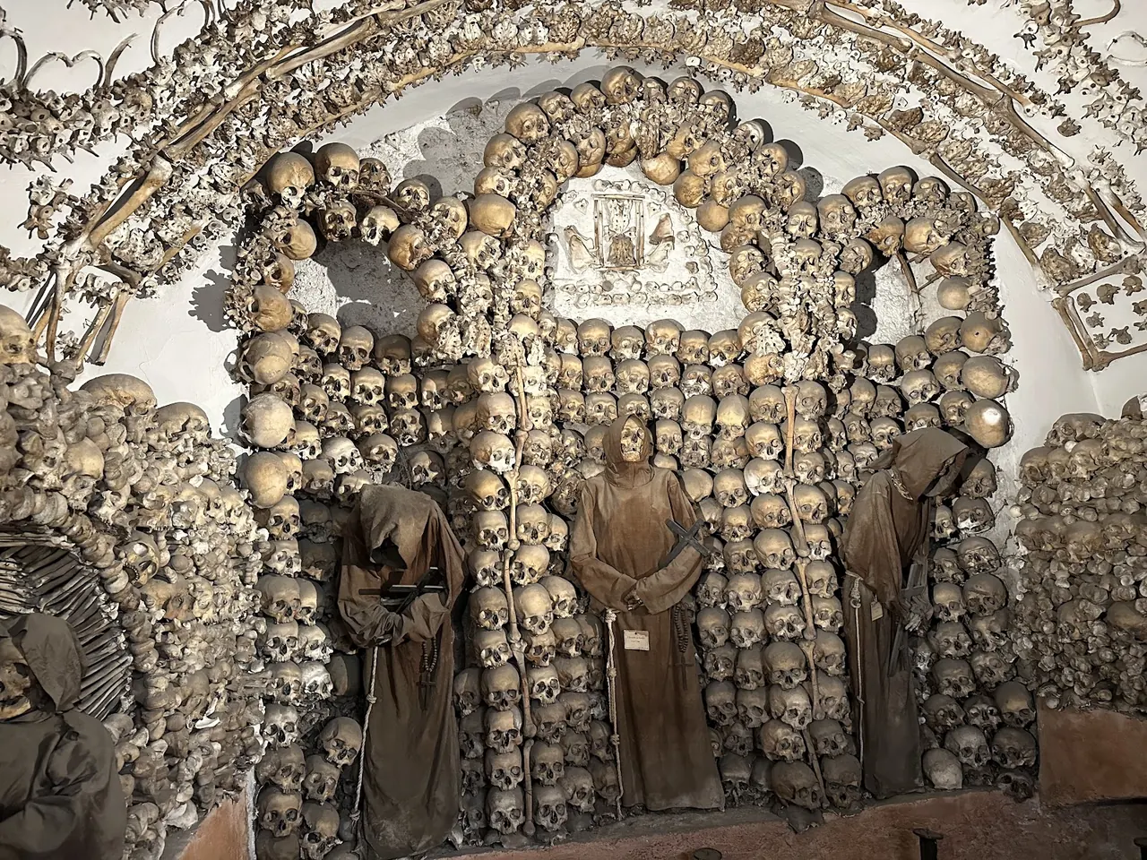 Arches built of skulls in the Capuchin Crypt in Rome, three robed friars standing in niches below