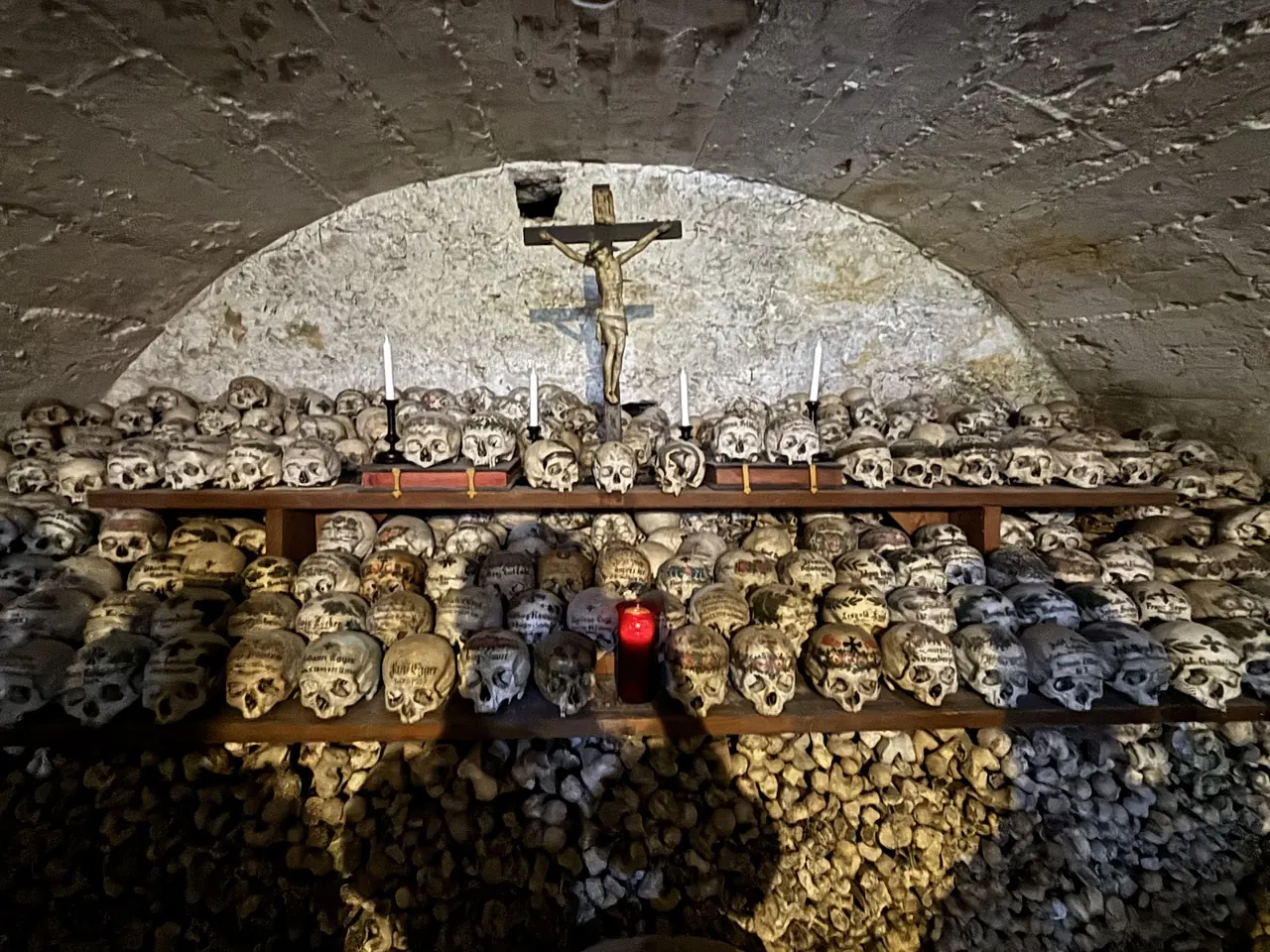 Shelves of painted skulls with names and flowers under a crucifix and candles in the Hallstatt Bone House