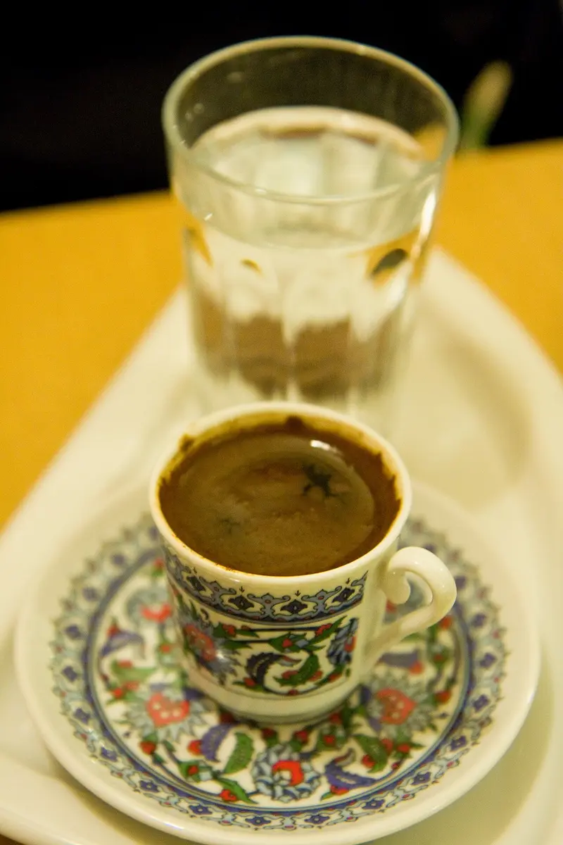 A patterned cup of Turkish coffee on a saucer, a glass of water behind it