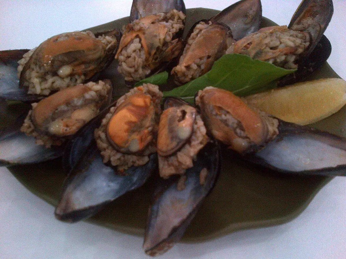A plate of mussels stuffed with spiced rice, with lemon wedges