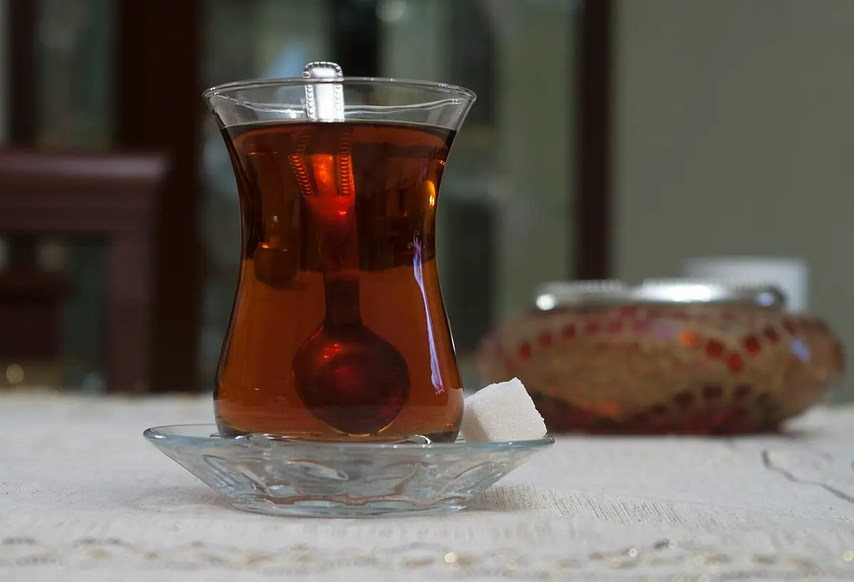 A tulip-shaped glass of black tea on a saucer with a sugar cube