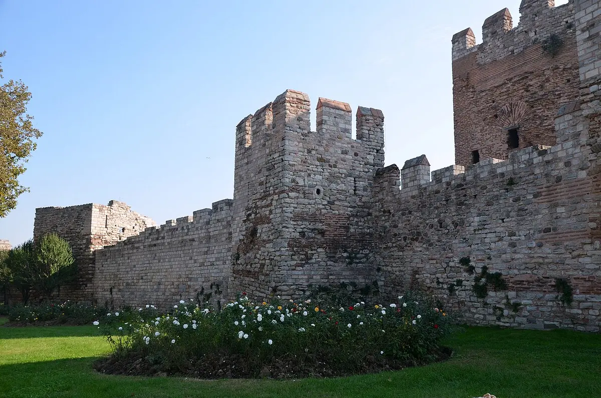 Towers and battlements of the Theodosian Walls against a blue sky, with a lawn in front