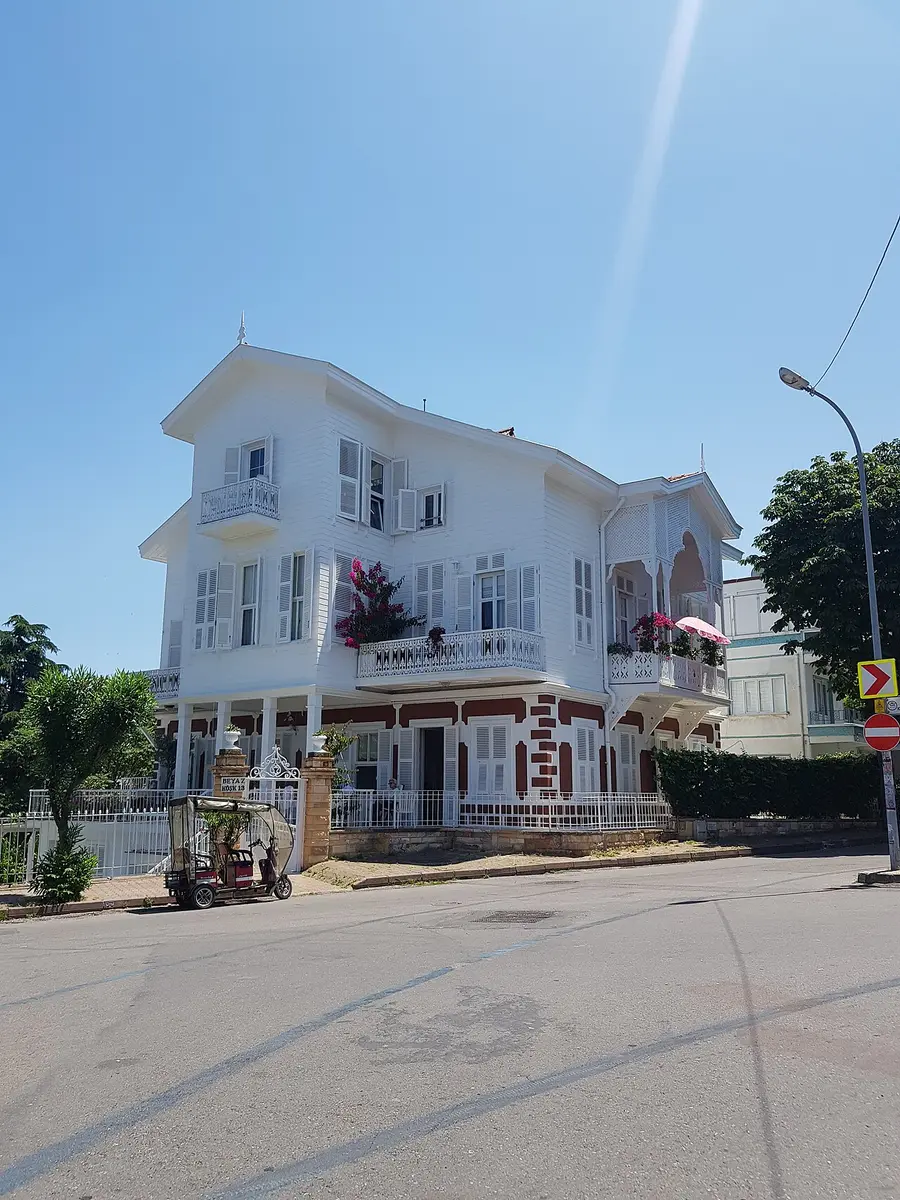 A white wooden mansion with balconies and flowers on a street corner on Büyükada