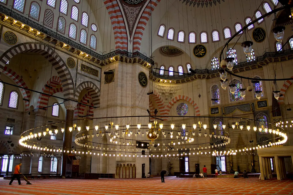 The prayer hall of the Süleymaniye Mosque, a wide ring of lamps hanging under the dome and rows of windows