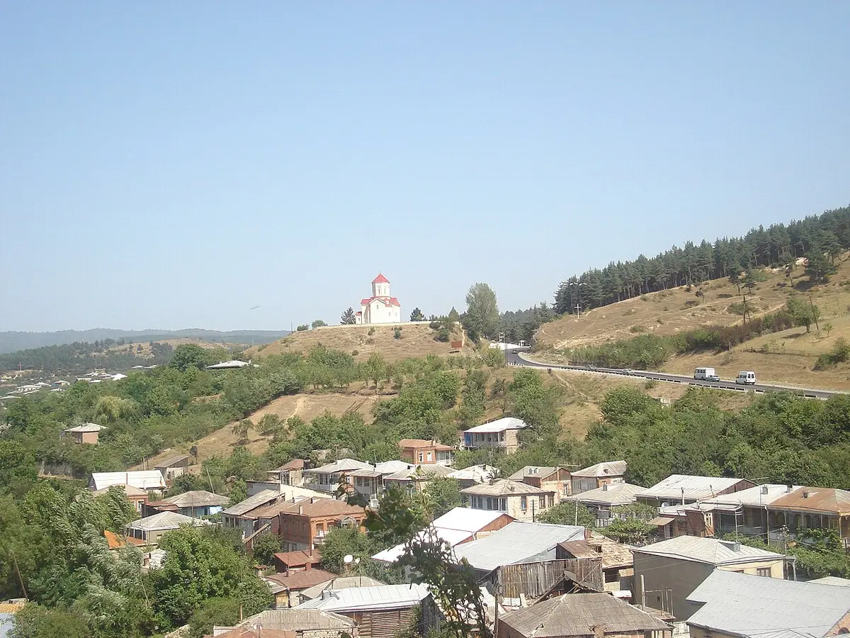 Houses of Surami among trees, with a church on a hill and pine-covered slopes behind