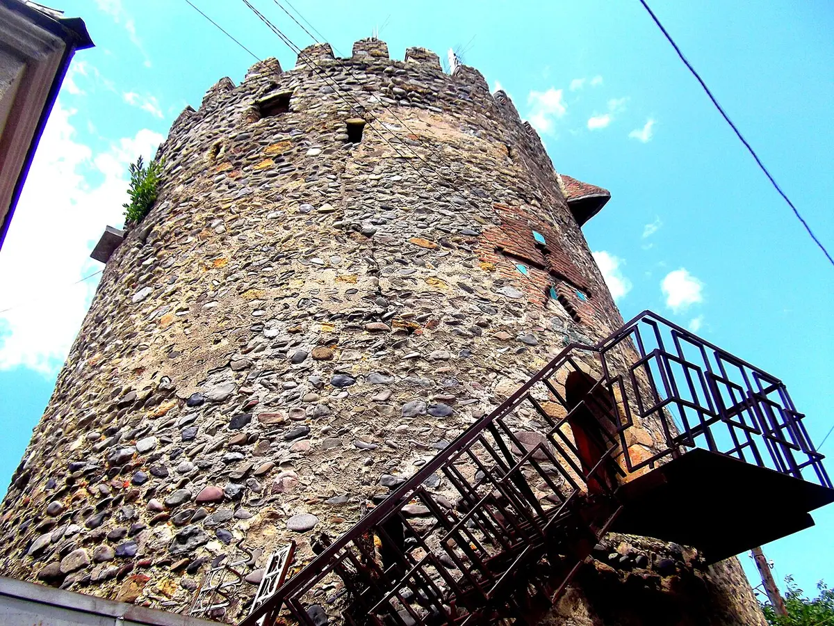 A round stone tower with crenellations and an iron staircase leading up to its door