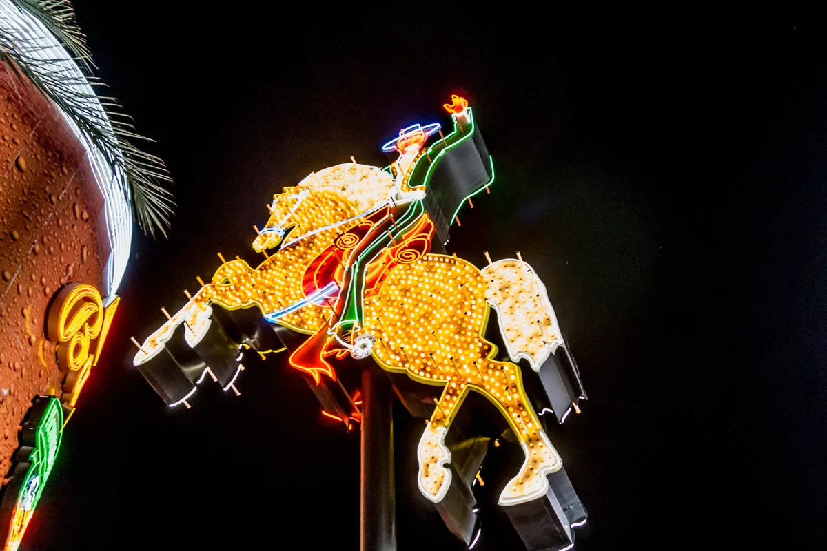 A neon sign of a cowboy on a rearing horse, outlined in yellow bulbs against the night sky