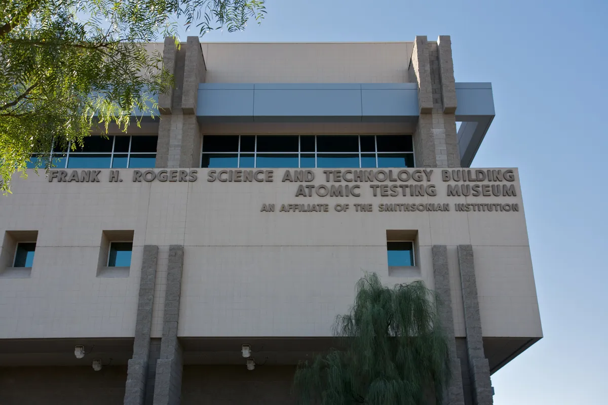 A concrete building front lettered Atomic Testing Museum and Frank H. Rogers Science and Technology Building, against a blue sky