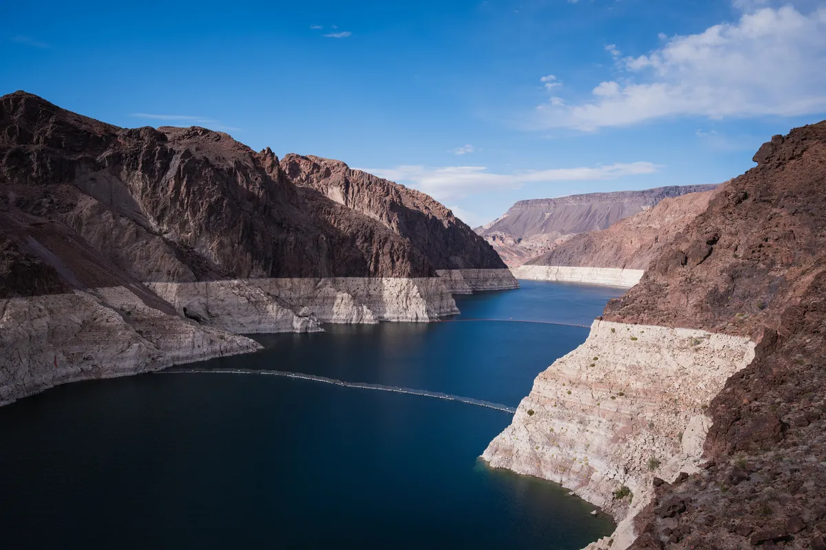 A deep blue arm of Lake Mead between dark canyon walls, a broad white band on the rock marking the old water line