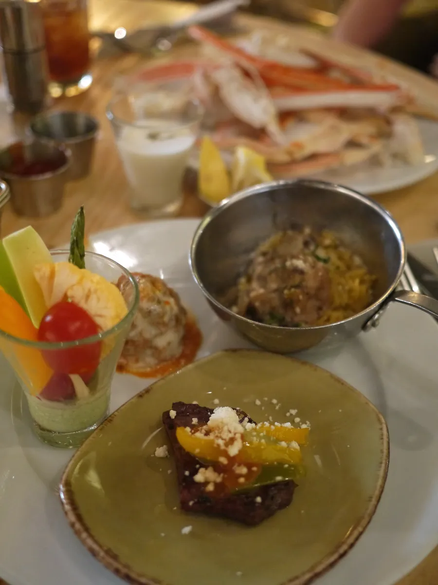Plates from a casino buffet on a table: crab legs, a cup of fruit, a small pan of rice and a slice of meat with peppers