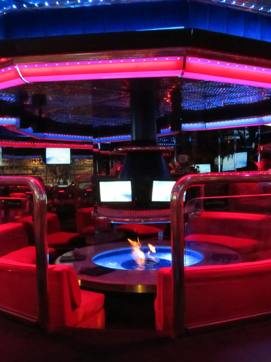 Red booths around a fire pit with blue flames under pink and blue neon in the Fireside Lounge