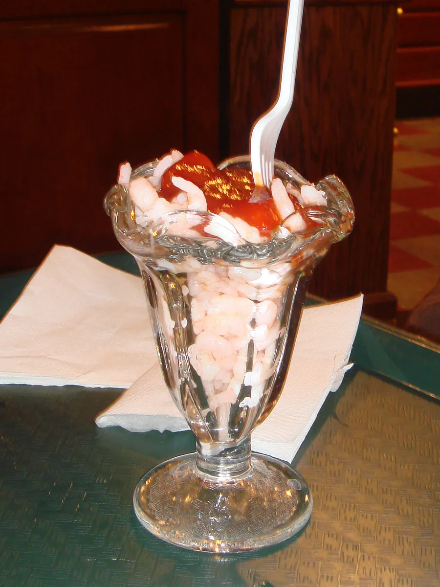 A tulip glass piled with small shrimp and red cocktail sauce, a plastic fork stuck in the top