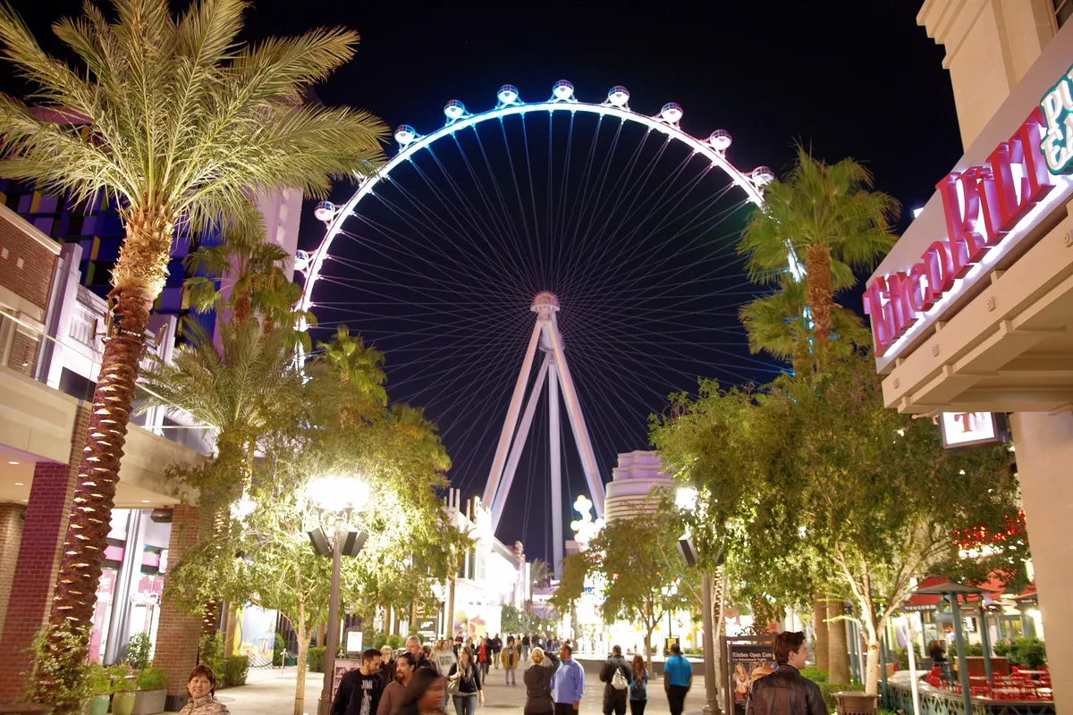 The High Roller observation wheel lit at night at the end of a palm-lined promenade