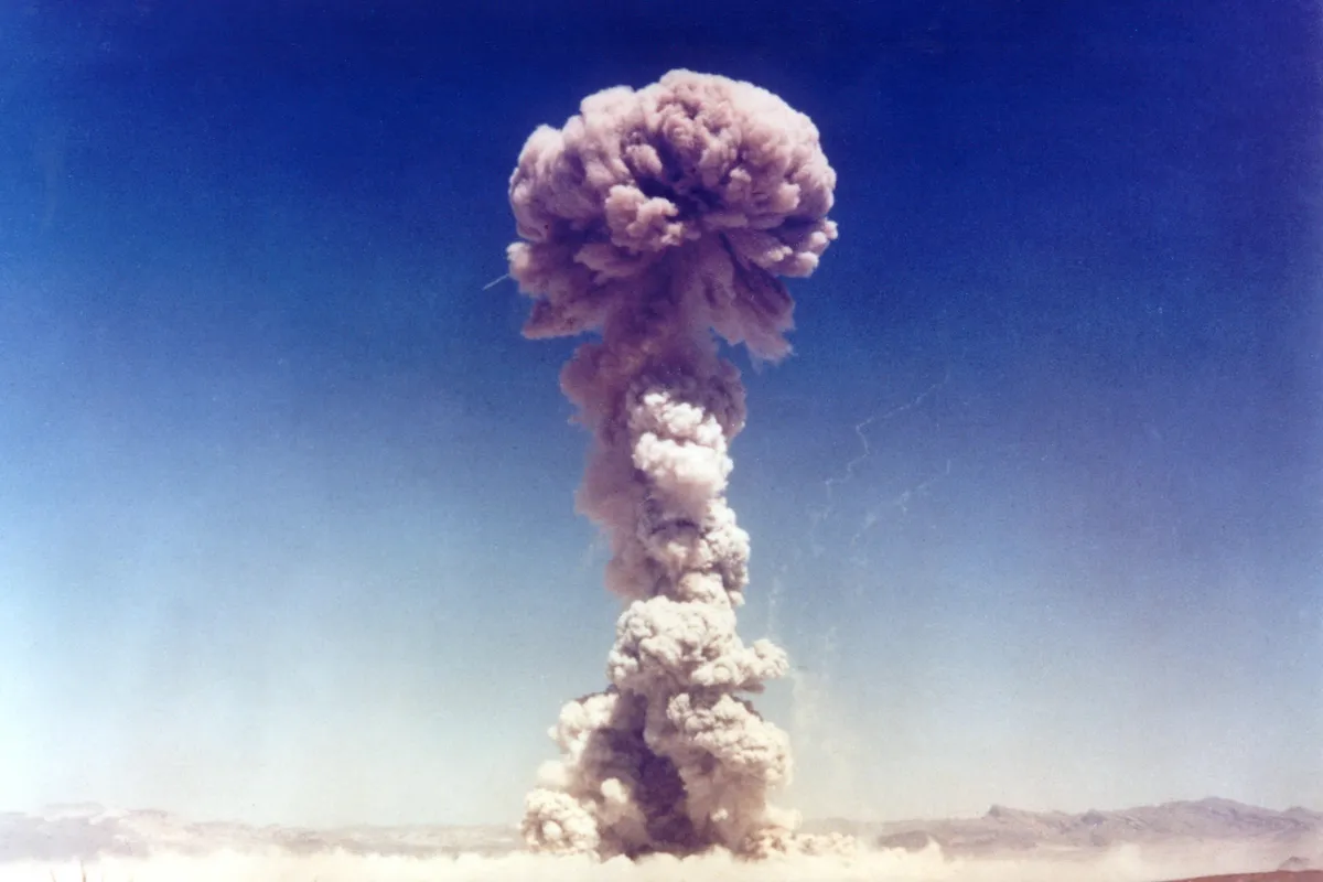 A tall mushroom cloud rising into a deep blue sky above the flat desert